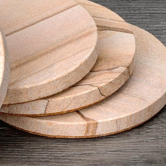Bare sandstone coasters stacked on dark wood, showing the natural banding across each cut face